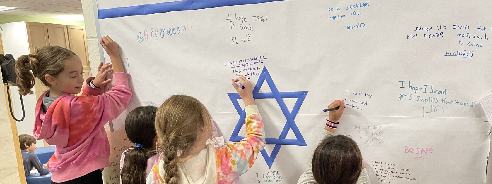 Girls writing prayers for Israel on Israeli flag bulletin board